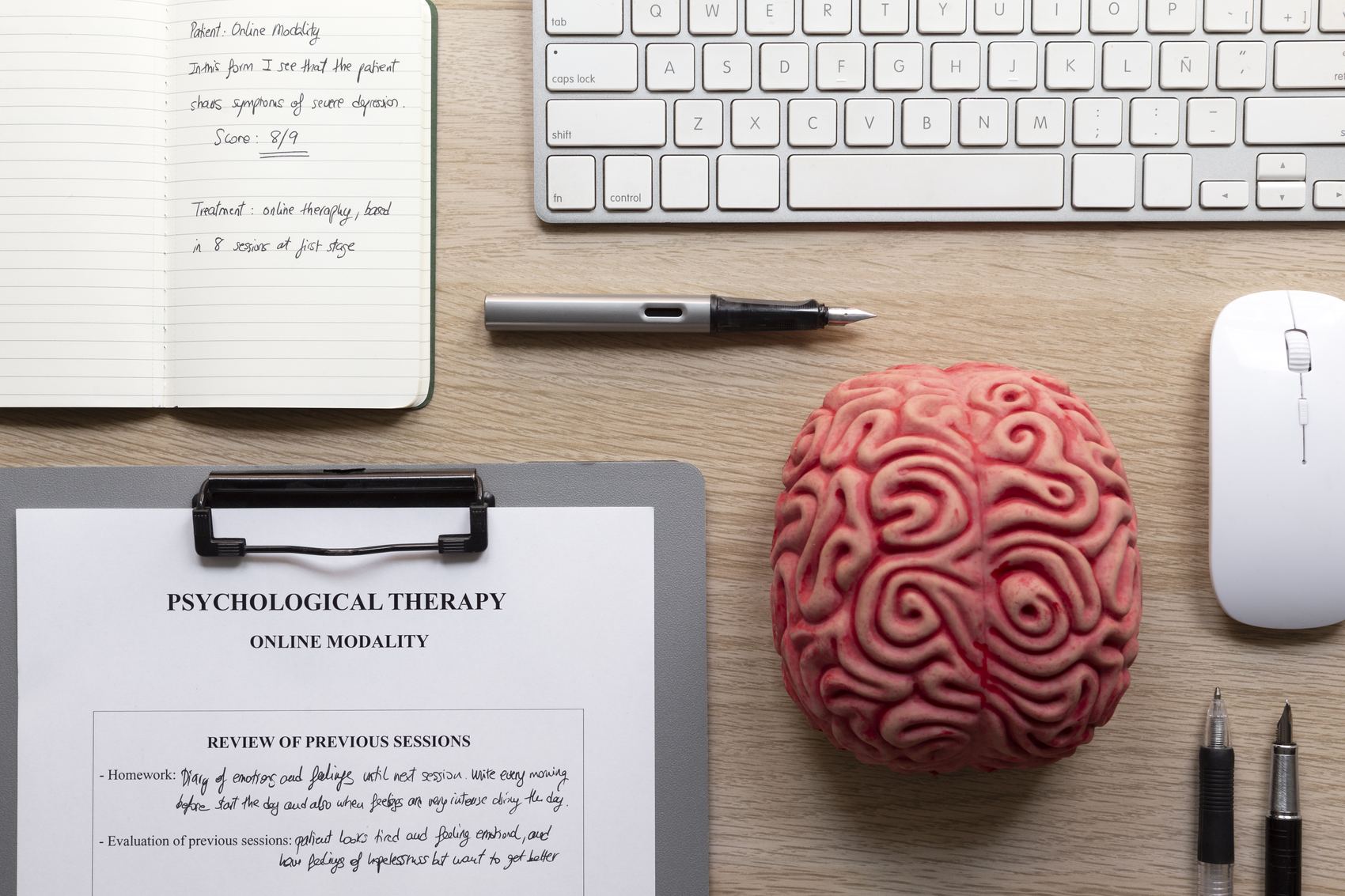 Bureau de consultation vu du dessus : carnet de notes, modèle de cerveau, clavier et grille d’évaluation.